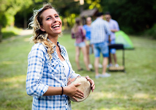 young woman playing a drum outside smiling